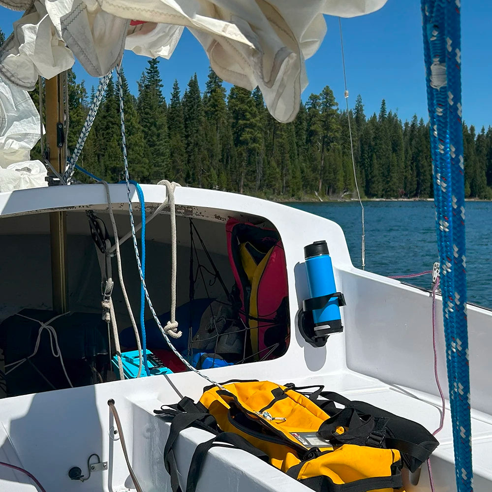 A TwistLock Vertical Mount attachable boat cup holder and blue insulated canteen attached to a sailboat on a beautiful mountain lake.