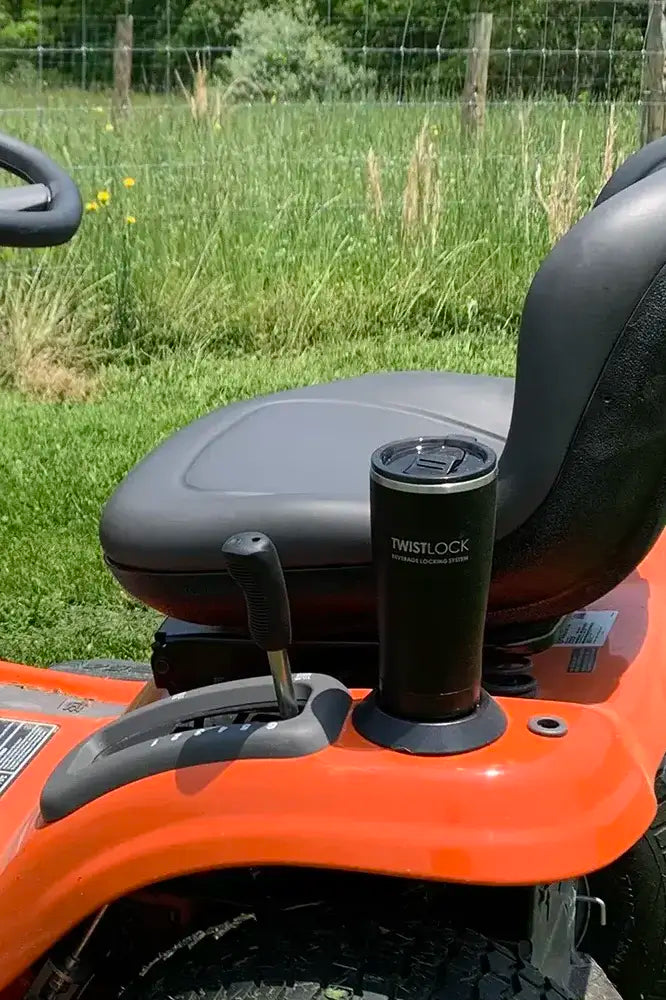 A driving lawnmower with an attachable upgrade cup holder on the fender with a stainless steel tumbler locked in.