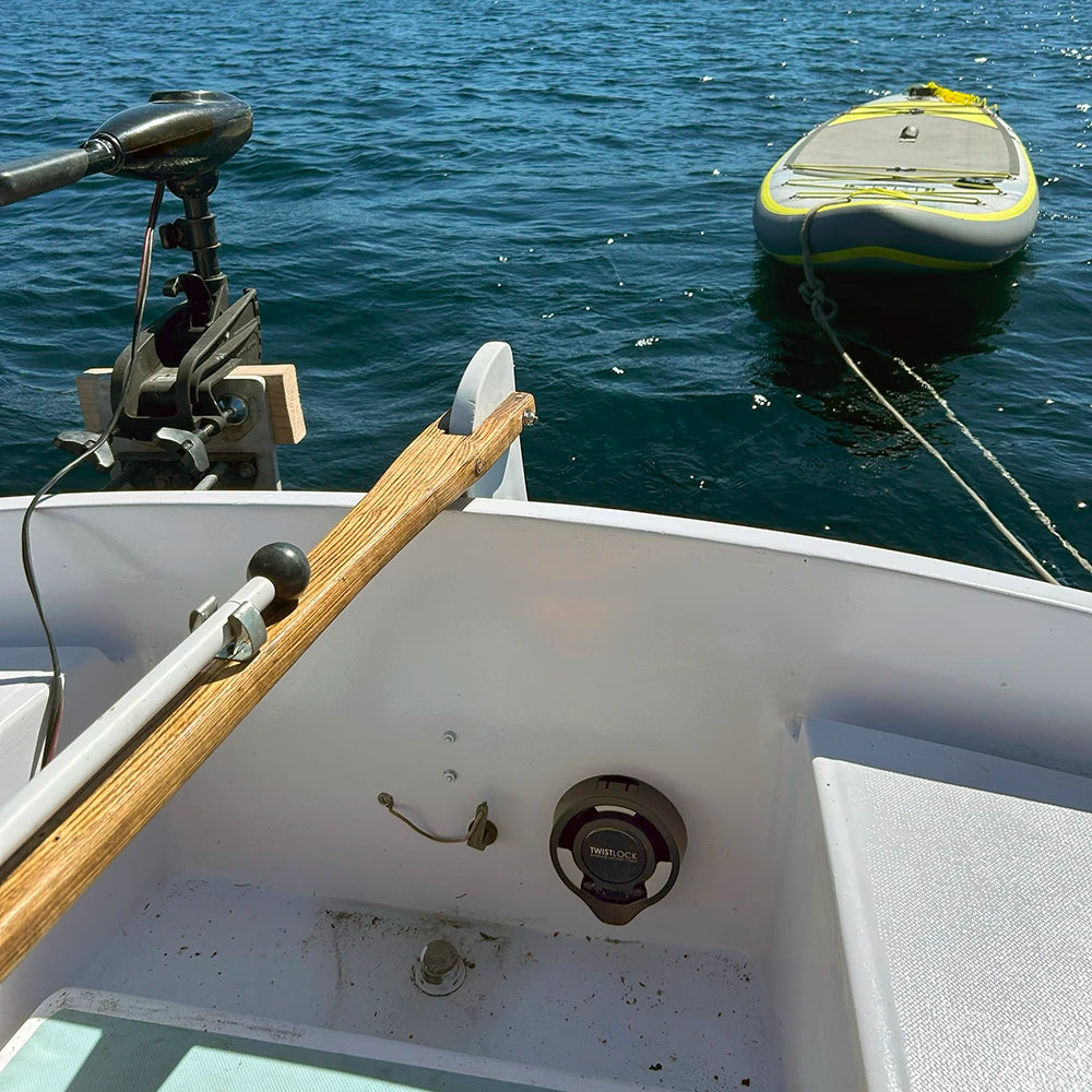 A sailboat tiller with a TwistLock attachable, folding vertically mounted marine cup holder with a paddleboarding floating behind.