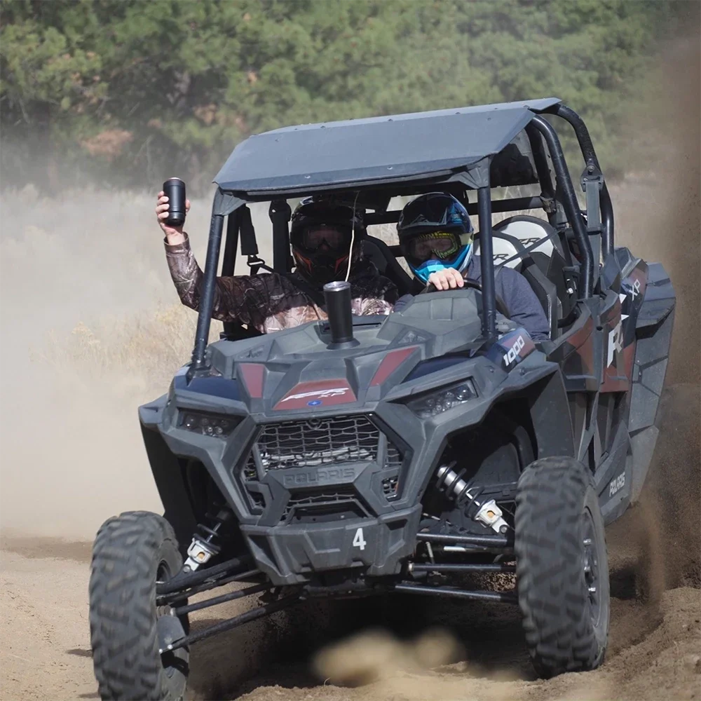 Side by side driving fast on a dirt road with the passenger lifting a drink out of the side.